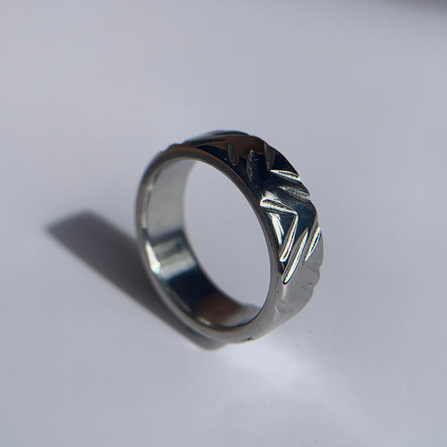 A silver-toned metal ring with a textured, hammered outer band and a polished inner band, standing upright on a light gray reflective surface.