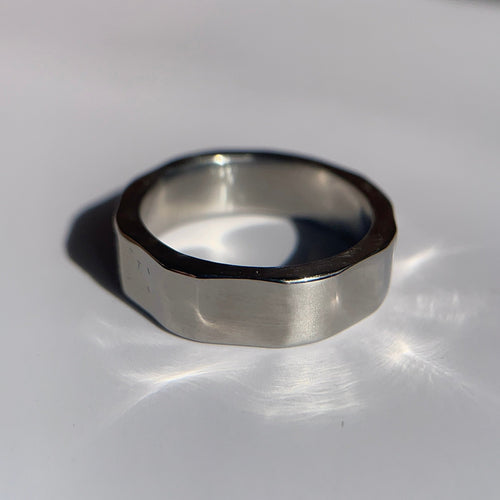 A silver-toned metal ring with a matte, textured octagonal band, resting on a white surface with a soft shadow.