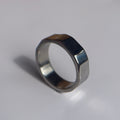 A silver-toned metal ring with a unique multi-sided, faceted band design, photographed on a plain light gray surface.