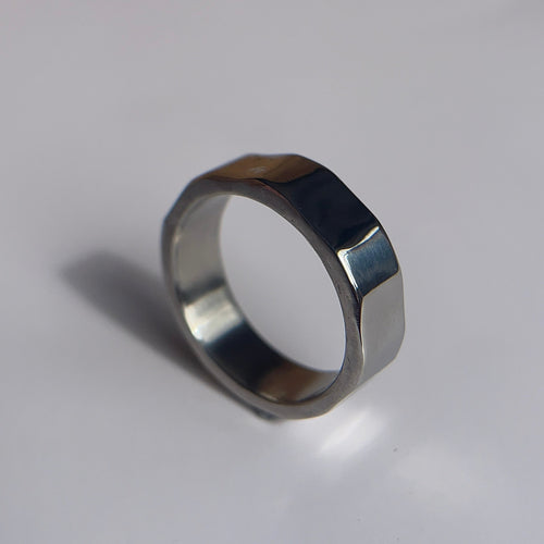 A silver-toned metal ring with a unique multi-sided, faceted band design, photographed on a plain light gray surface.