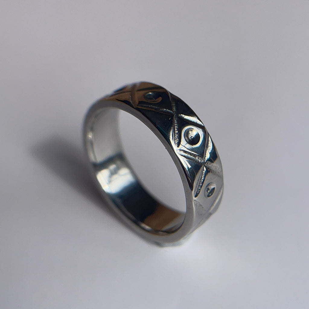 A silver band ring with a textured, hammered geometric pattern, photographed on a plain light gray surface.