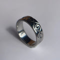 A silver band ring with a textured, hammered geometric pattern, photographed on a plain light gray surface.