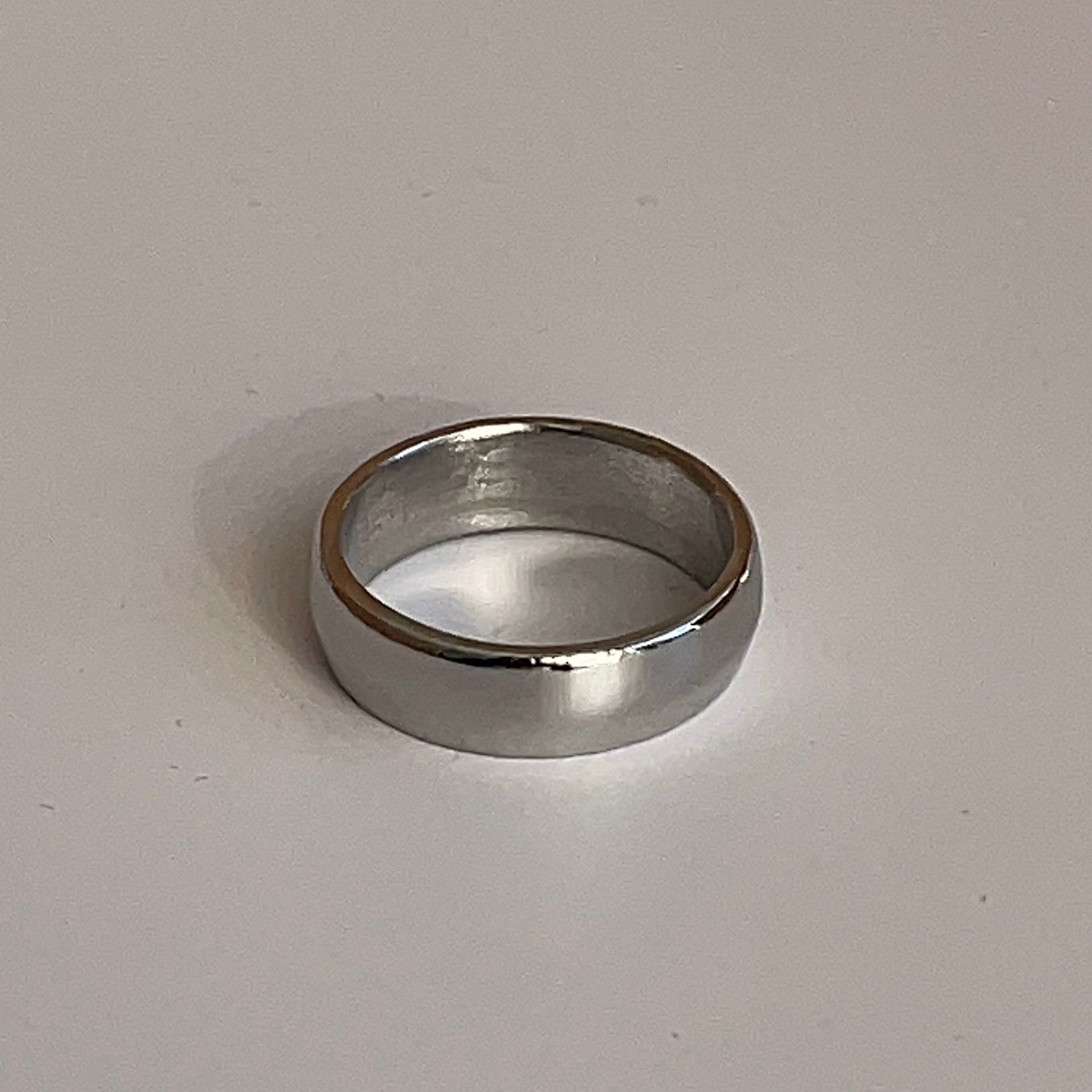A simple silver metal band ring with a matte finish, photographed on a plain light gray surface.