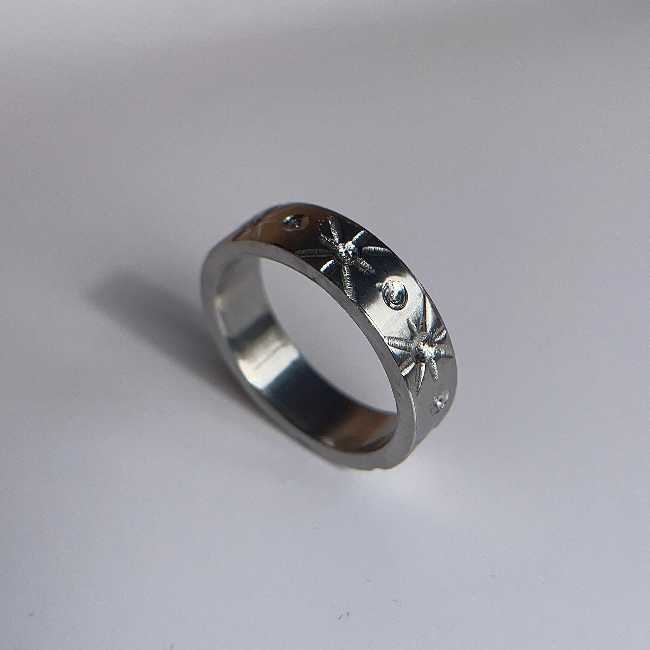 A silver band ring with engraved starburst patterns on its outer surface, photographed on a plain light gray background.