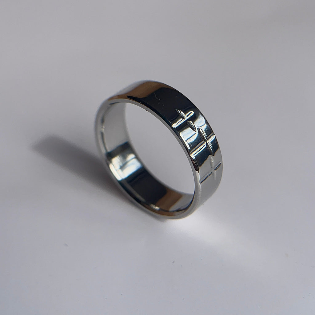 A polished silver band ring with engraved Hebrew lettering, resting on a plain white surface.